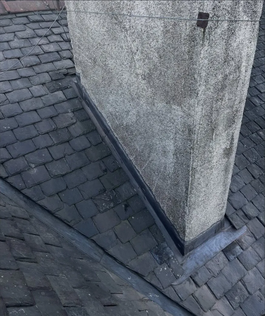 Fresh lead flashing dressed round a stone chimney stack on a slate roof